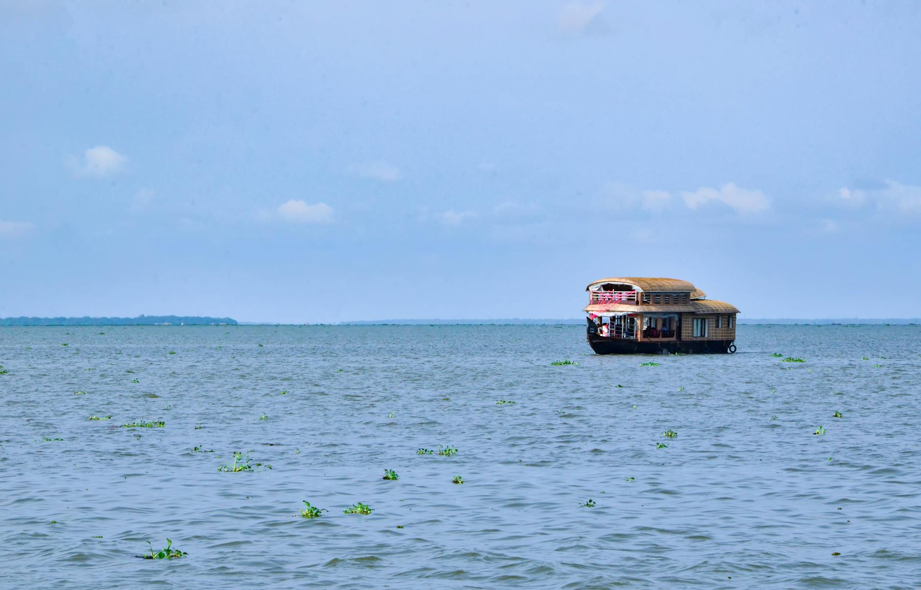 Traditional Kerala houseboat gliding through calm backwater canals lined with lush green palm trees.